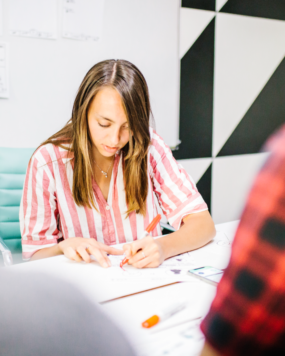 Fiona at a desk, sketching with a red pen on printed wireframes